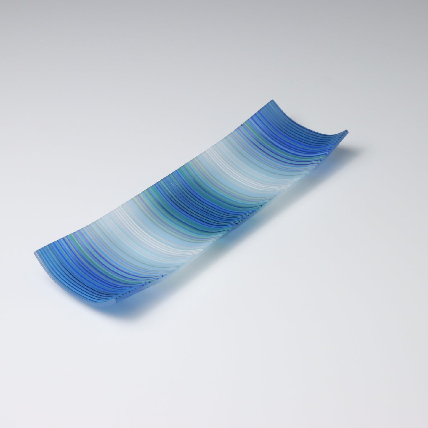 A decorative shallow rectangular boat shaped glass plate with raised corners and a  colourful ColourWave stripe patterns showing key colours of blue, green and white