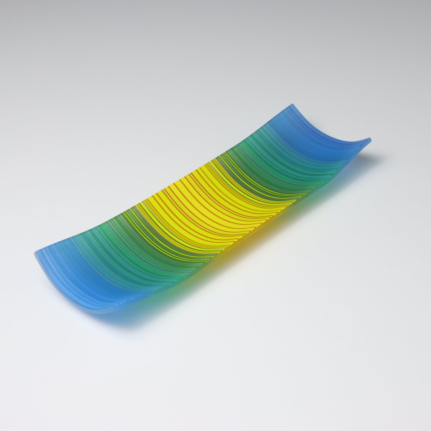 A decorative shallow rectangular boat shaped glass plate with raised corners and a  colourful ColourWave stripe patterns showing key colours of bright blues, greens and yellow