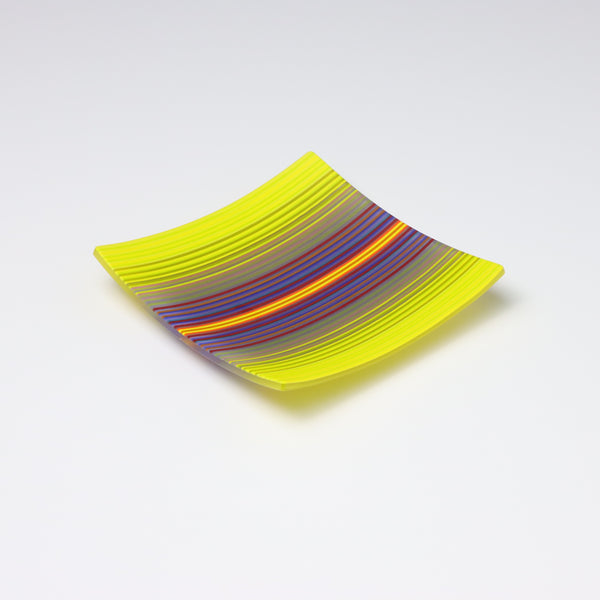 A decorative square shallow glass plate with raised corners and a  colourful ColourWave stripe patterns showing key colours of yellow, and purple, blue  and red.