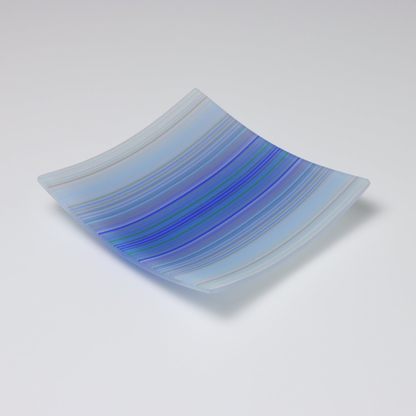 A decorative square shallow glass plate with raised corners and a  colourful ColourWave stripe patterns showing key colours of pale blues, lilac and darker blues in the center