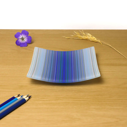 A decorative square shallow glass plate with raised corners and a  colourful ColourWave stripe patterns showing key colours of pale blues, lilac and darker blues in the center