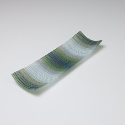A decorative shallow rectangular boat shaped glass plate with raised corners and a  colourful ColourWave stripe patterns showing key colours of white, grey with underlying colours of green and pale blue