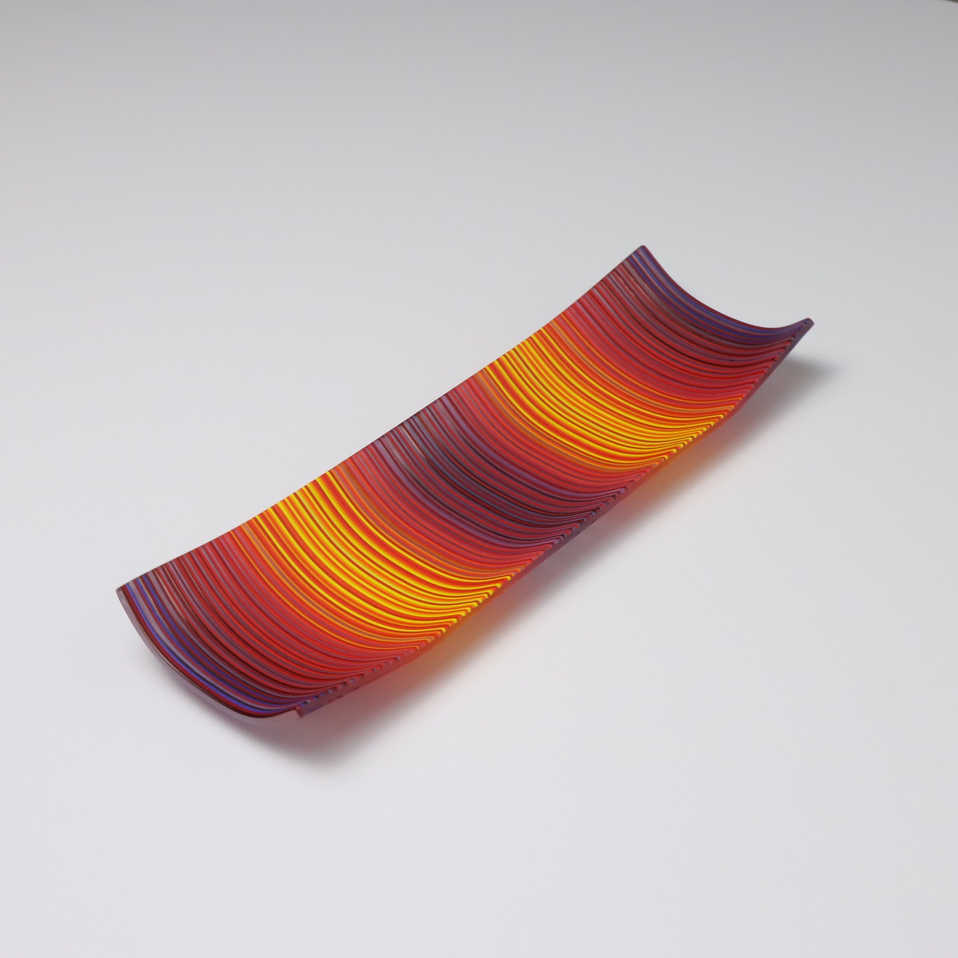 A decorative shallow rectangular boat shaped glass plate with raised corners and a  colourful ColourWave stripe patterns showing key colours of purple and orange and yellow