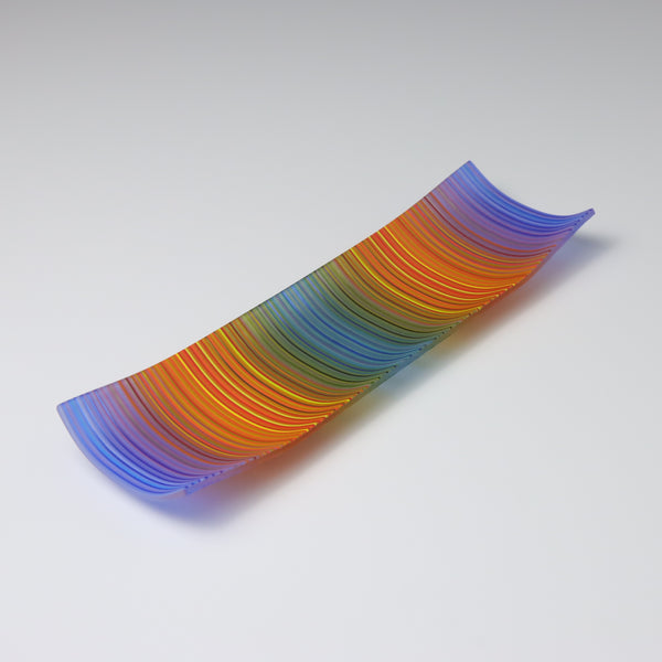 A decorative shallow rectangular boat shaped glass plate with raised corners and a  colourful ColourWave stripe patterns showing key colours of blue, orange and teal