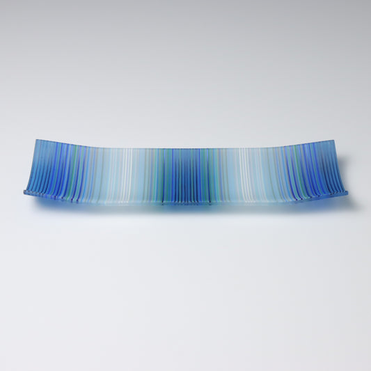 A colourful decorative fused glass small boat shaped plate that curves up at the corners. This piece has a ColourWave design, made from fine strands of glass known as stringers, that starts and ends in blue bands of colour and transitions to white, with a blue center. 