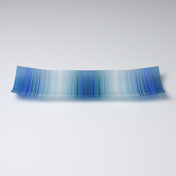 A colourful decorative fused glass small boat shaped plate that curves up at the corners. This piece has a ColourWave design, made from fine strands of glass known as stringers, that starts and ends in blue bands of colour and transitions to white, with a blue center. 