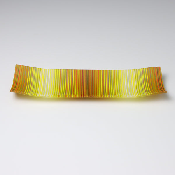 A colourful decorative fused glass small boat shaped plate that curve up at the corners. This piece has a ColourWave design, made from fine strands of glass known as stringers From a distance the bands of colours look golden yellow and transitions to a paler yellows and back agiain.  Close up the waves of colours are made up of many different colours 