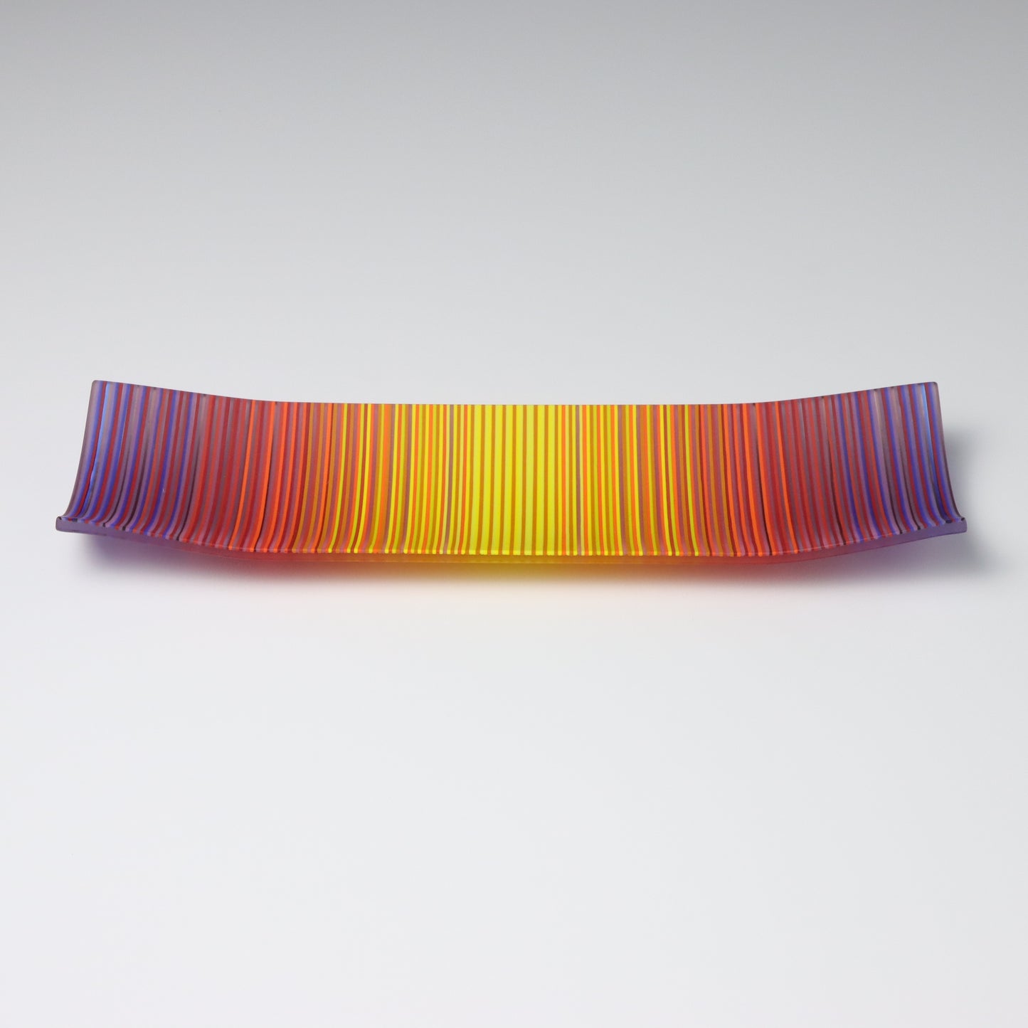 A decorative shallow rectangular boat shaped glass plate with raised corners and a  colourful ColourWave stripe patterns showing key colours of purple, red and yellow.