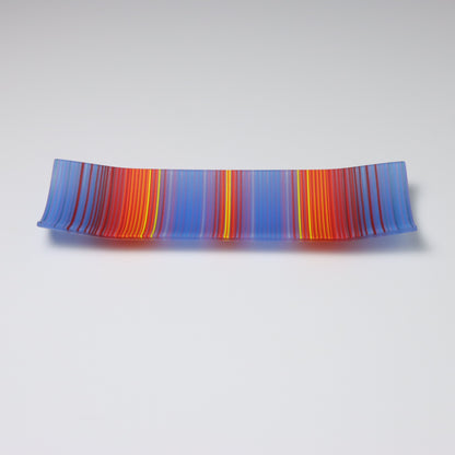 A decorative rectangular glass plate with raised corners and coloured stripe patterns showing key colours of bold blue, red and yellow 