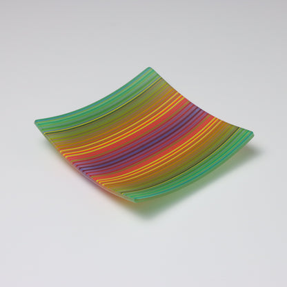 A decorative square shallow glass plate with raised corners and a  colourful ColourWave stripe patterns showing key colours of green, yellow, red and blue