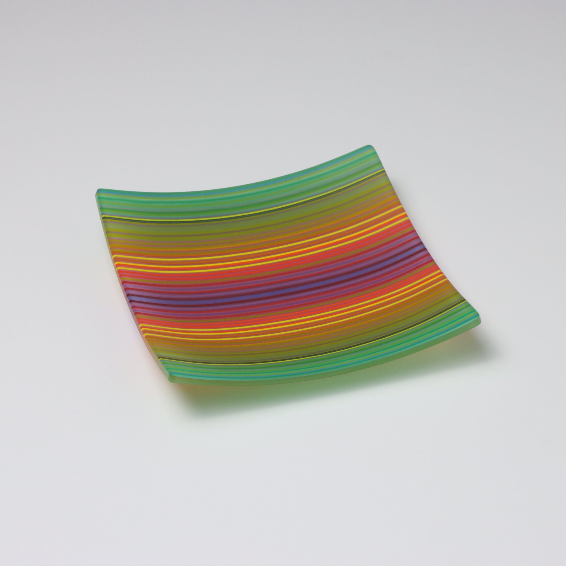 A decorative square shallow glass plate with raised corners and a  colourful ColourWave stripe patterns showing key colours of green, yellow, red and blue