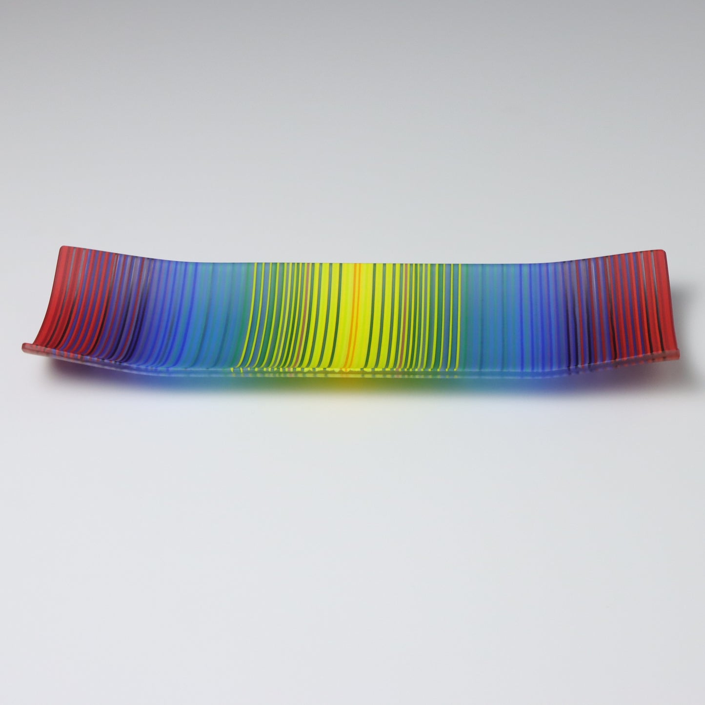 A decorative shallow rectangular boat shaped glass plate with raised corners and a  colourful ColourWave stripe patterns showing key colours of bold red, blue, green and yellow