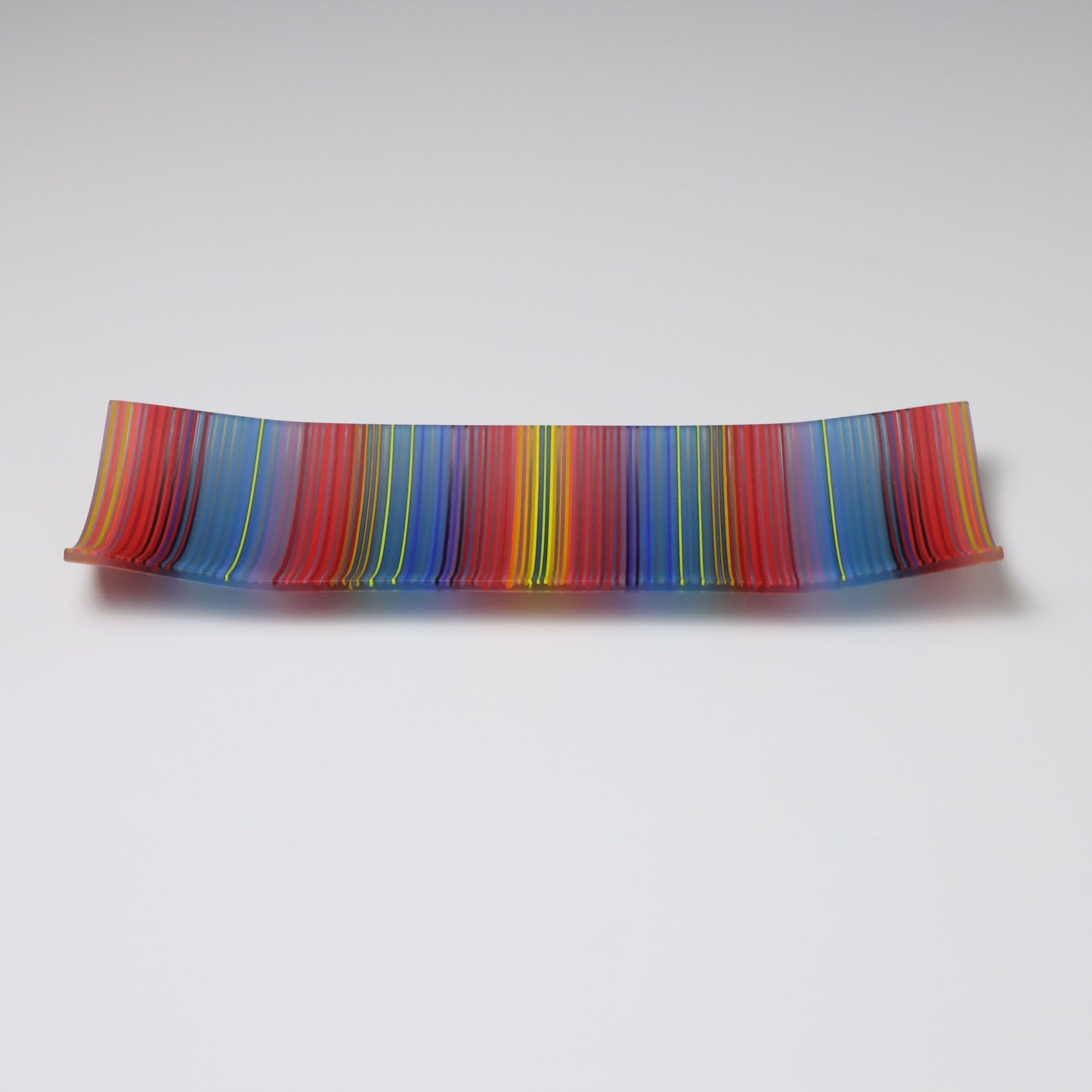 A decorative shallow rectangular boat shaped glass plate with raised corners and a  colourful ColourWave stripe patterns showing key colours of blue, red and green highlights