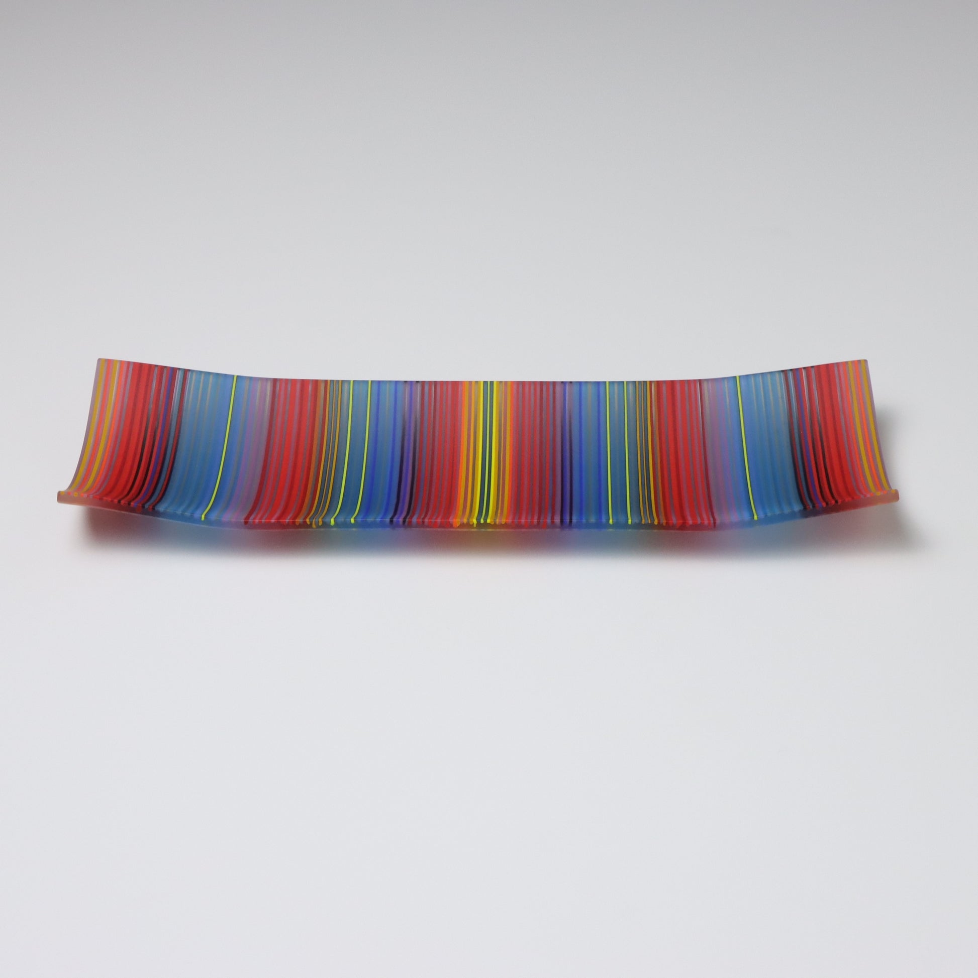 A decorative shallow rectangular boat shaped glass plate with raised corners and a  colourful ColourWave stripe patterns showing key colours of blue, red and green highlights