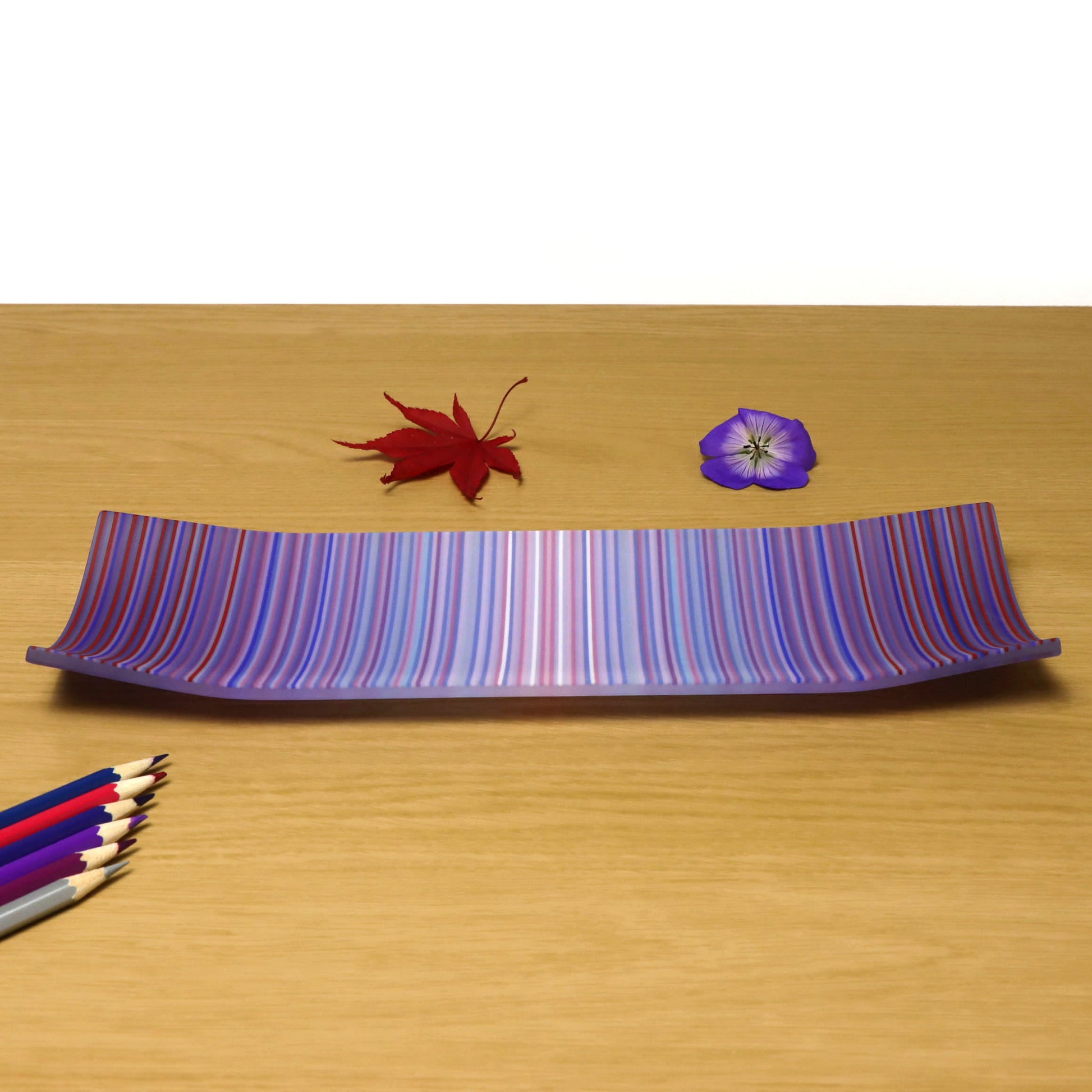 A decorative shallow rectangular boat shaped glass plate with raised corners and a  colourful ColourWave stripe patterns showing key colours of purple, pale blue and pink