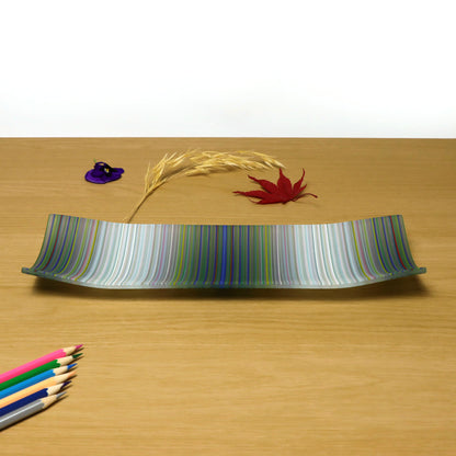 A decorative shallow rectangular boat shaped glass plate with raised corners and a  colourful ColourWave stripe patterns showing key colours of white, grey with underlying colours of green and pale blue