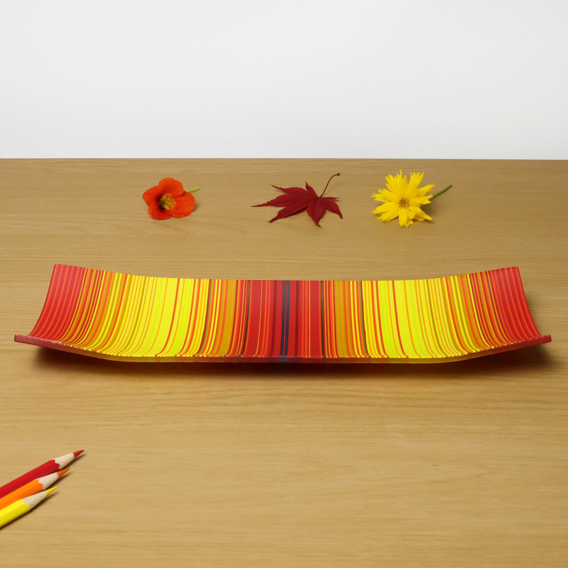 A decorative shallow rectangular boat shaped glass plate with raised corners and a  colourful ColourWave stripe patterns showing key colours of fiery reds and bright yellows