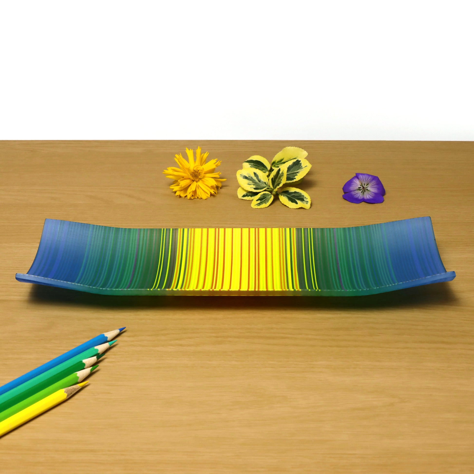 A decorative shallow rectangular boat shaped glass plate with raised corners and a  colourful ColourWave stripe patterns showing key colours of bright blues, greens and yellow
