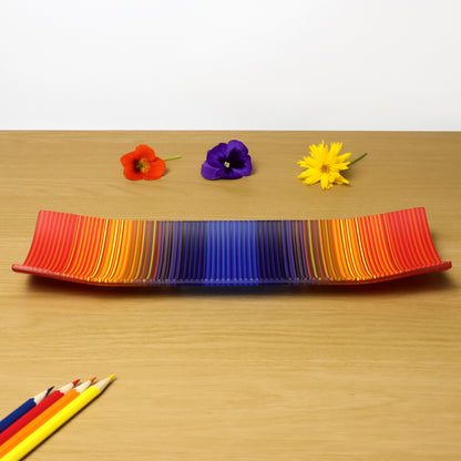 A decorative shallow rectangular boat shaped glass plate with raised corners and a  colourful ColourWave stripe patterns showing key colours of red, yellow and blue.